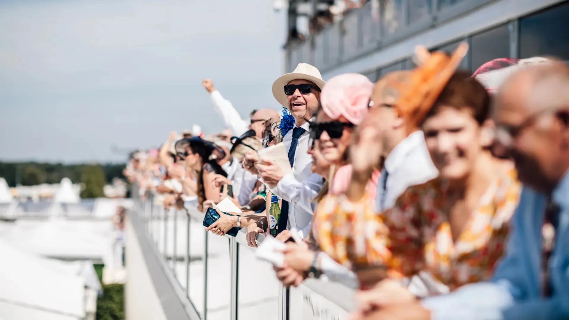 Guests in summer dresses and hats leaning over the rail of the Lawn Club at Ascot to watch the racing.