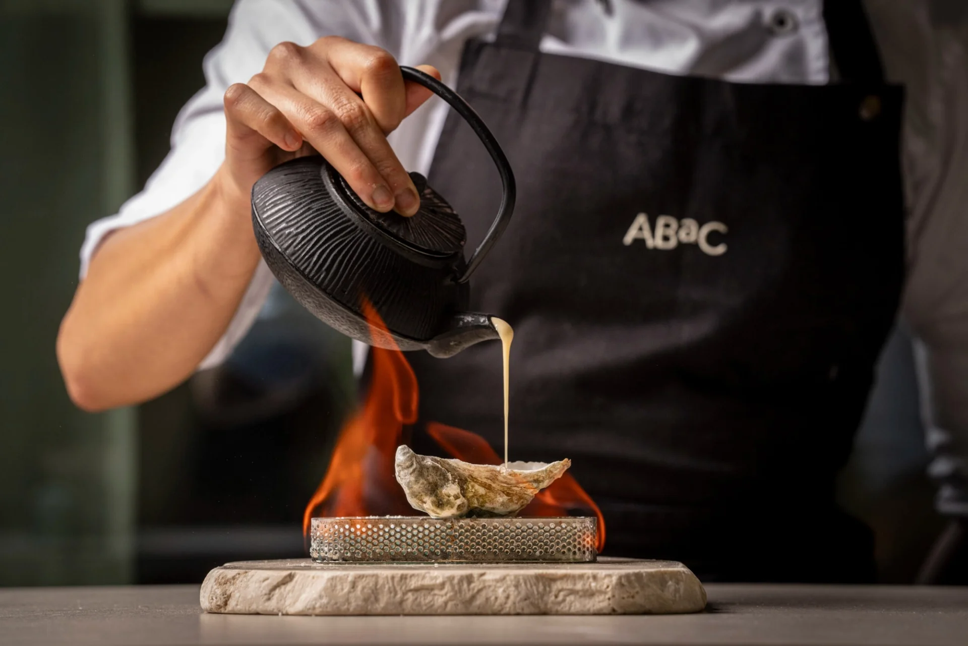 A chef pours sauce over a shell above flames at ABaC.