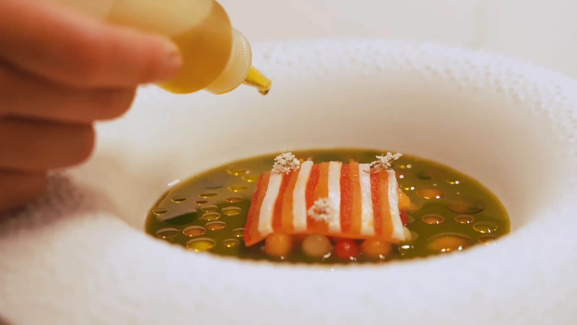 A hand finishes a colourful striped tasting-menu dish with drops of oil at Mirazur.