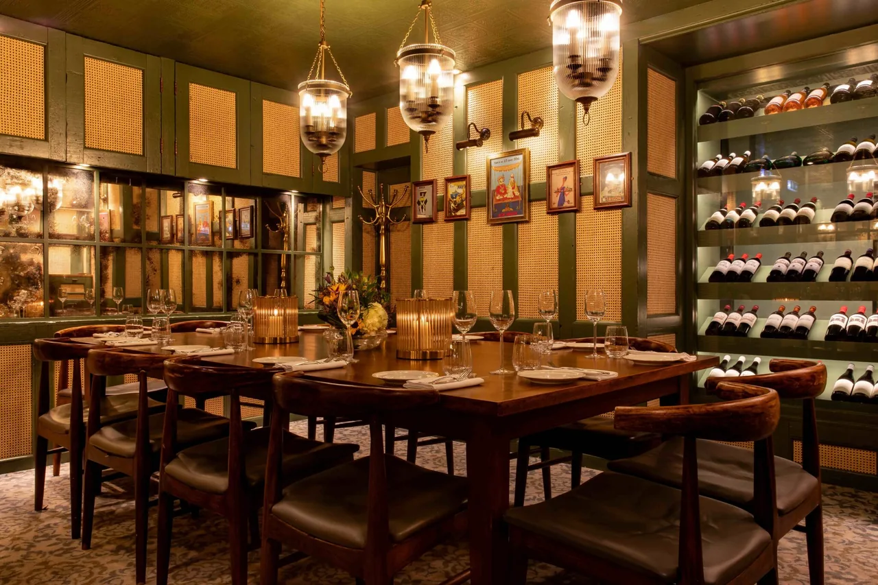 Warmly lit dining tables, cane wall panels and a wine display at Trishna