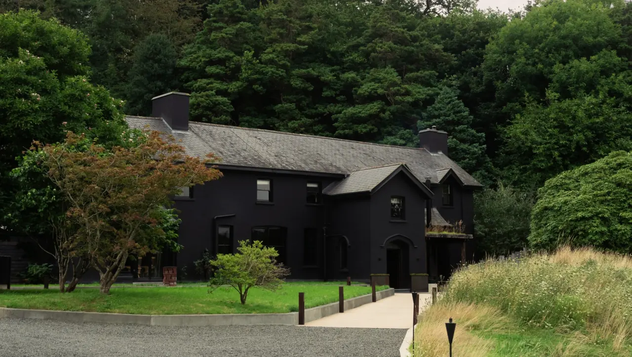 The black-painted exterior of Ynyshir surrounded by trees and gardens