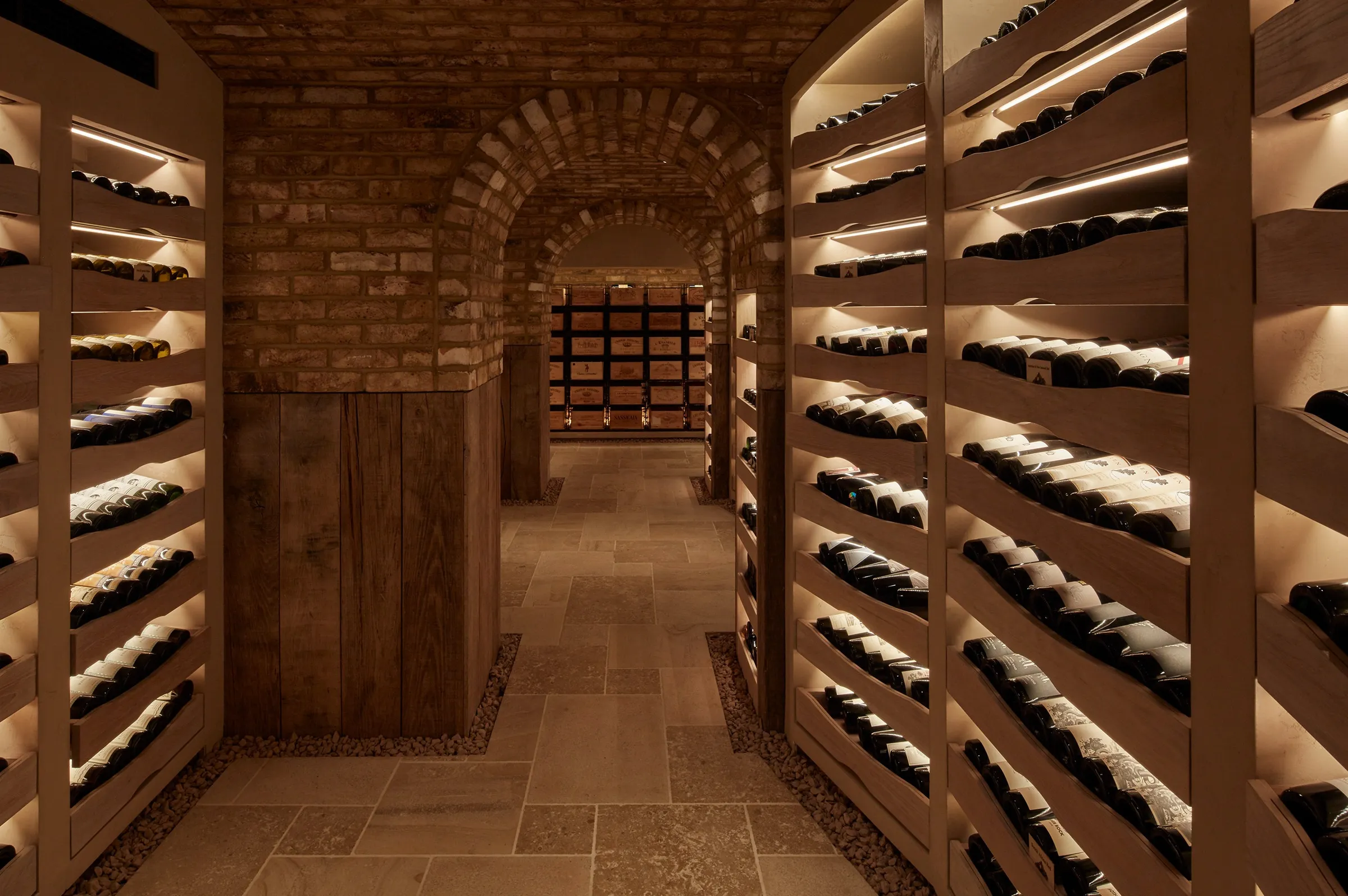 The brick-vaulted wine cellar at HIDE in Mayfair, bottles lying on lit timber shelves either side of a stone-flagged walkway.