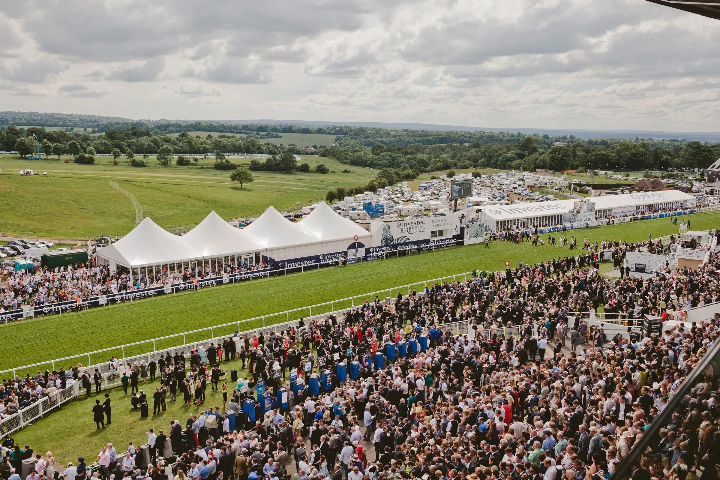 Crowds along the rail at Epsom, with white marquees and open downland stretching away behind.