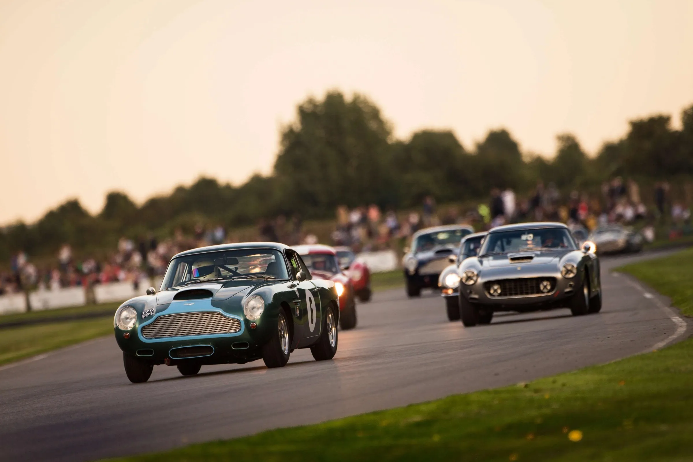 Period sports cars racing wheel to wheel at the Goodwood Revival in low evening sun.