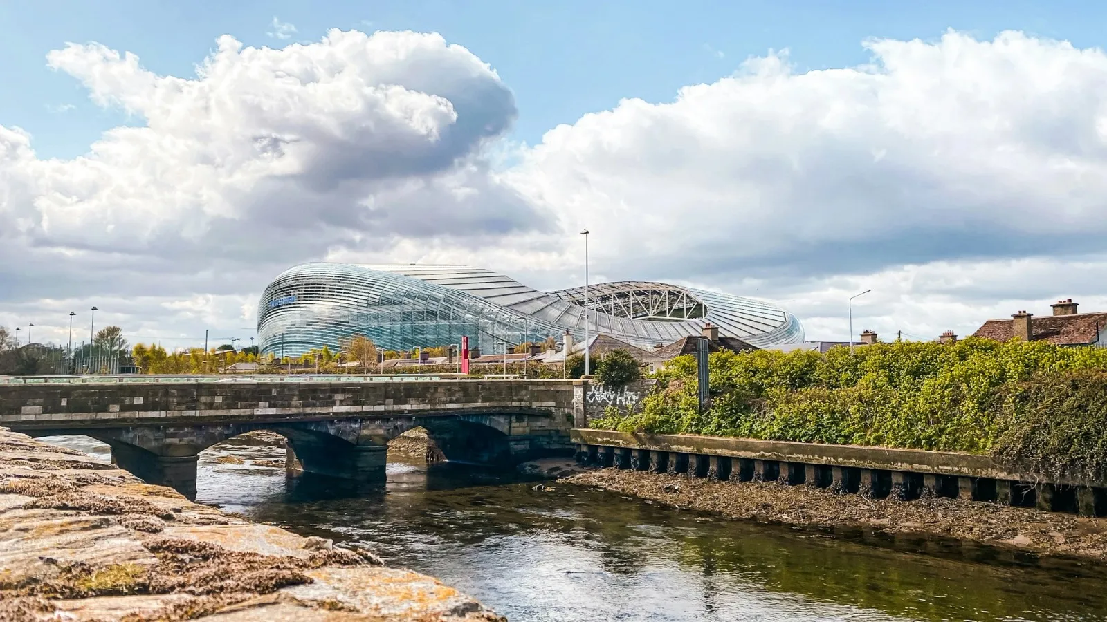 The Aviva Stadium in Dublin, seen across a river and an old stone bridge.