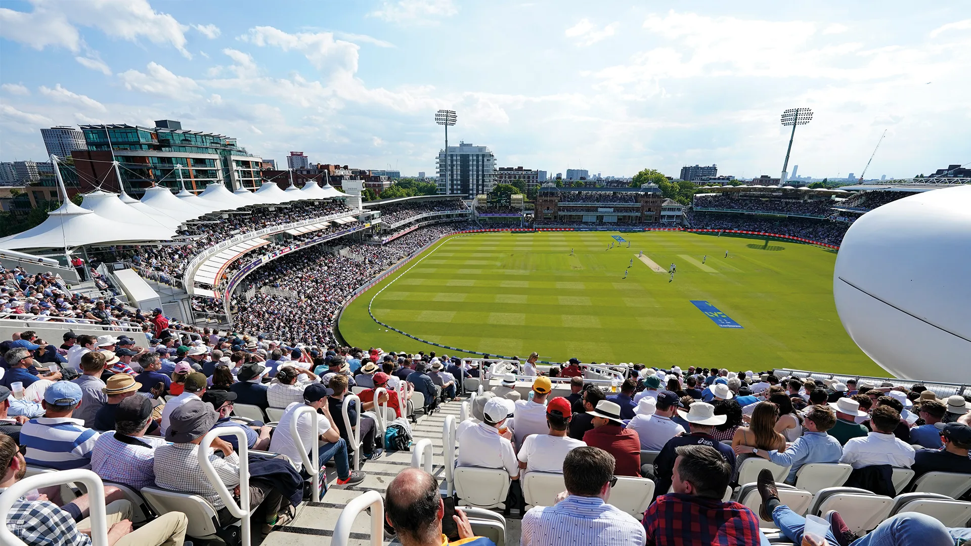 Spectators filling the stands at Lord’s on a sunny day’s play, with the Pavilion on the far side of the ground.