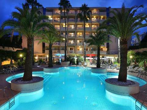 Image of hotel with outdoorpool and palm trees, lit up at night