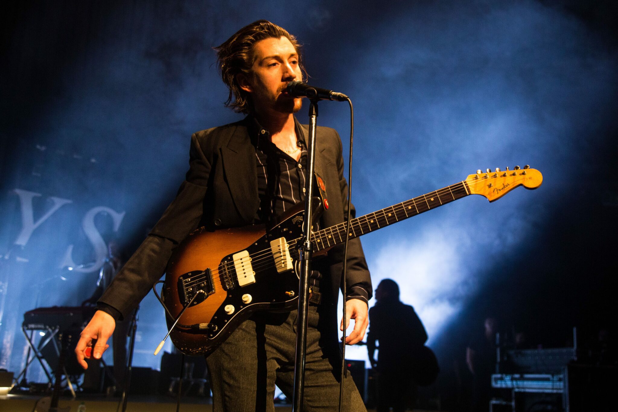 A close up shot of Alex Turner from the Arctic Monkeys with his guitar performing live