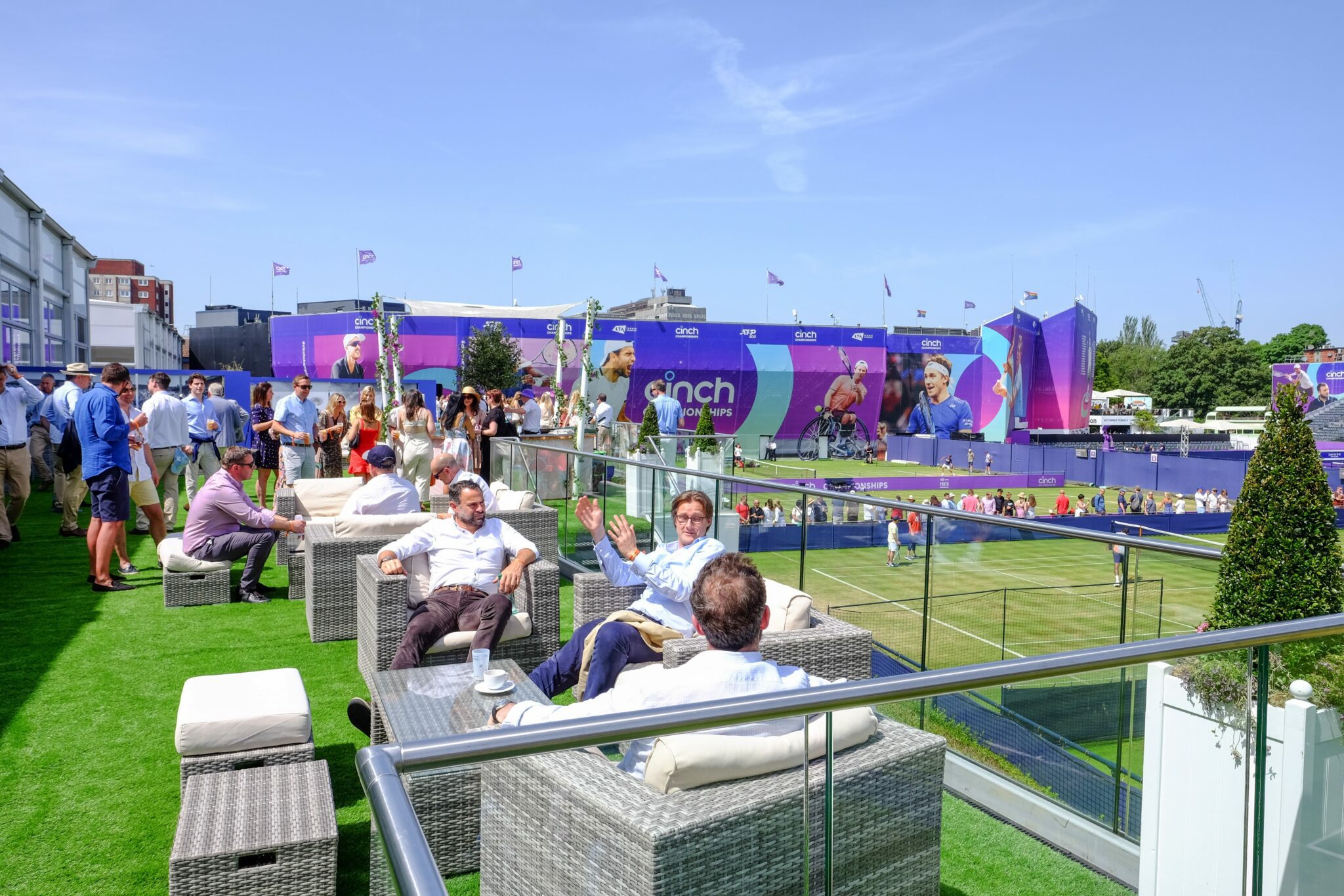 Image of the rooftop garden at The Queens Club with guests sat on outdoor chairs overlooking the game
