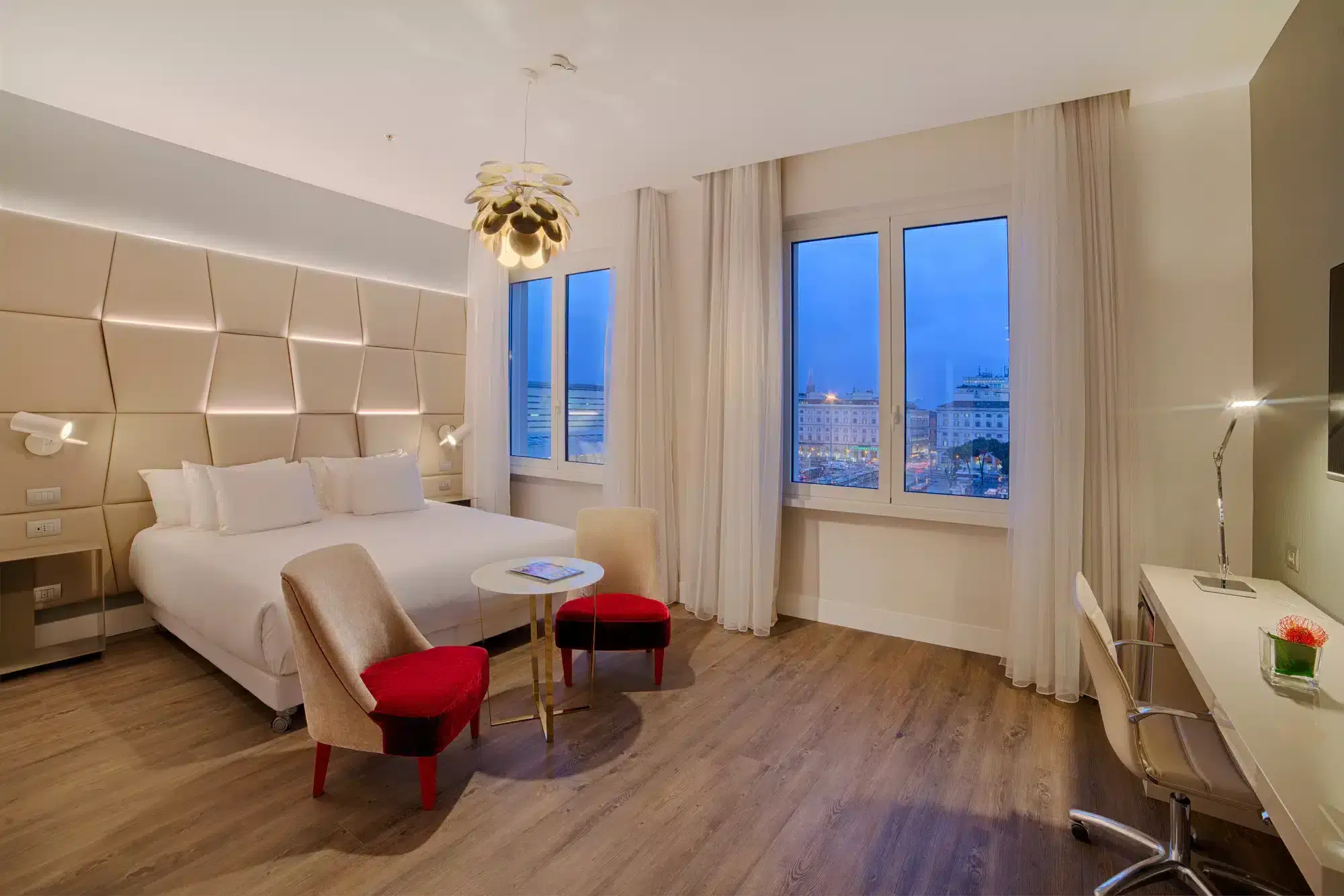 Image of a hotel room with a large double bed, red seating and a large window looking out to the night sky