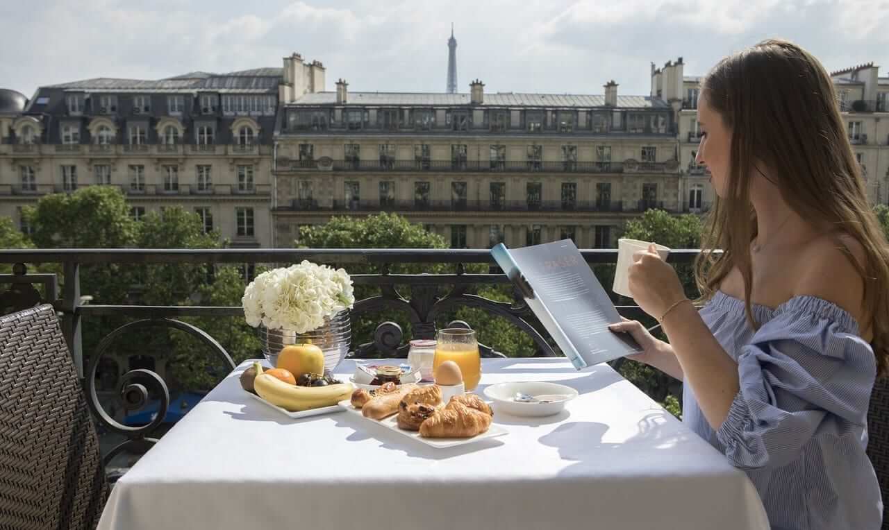 Image of lady drinking coffee and having a continental breakfast on her balcony whilst reading a book