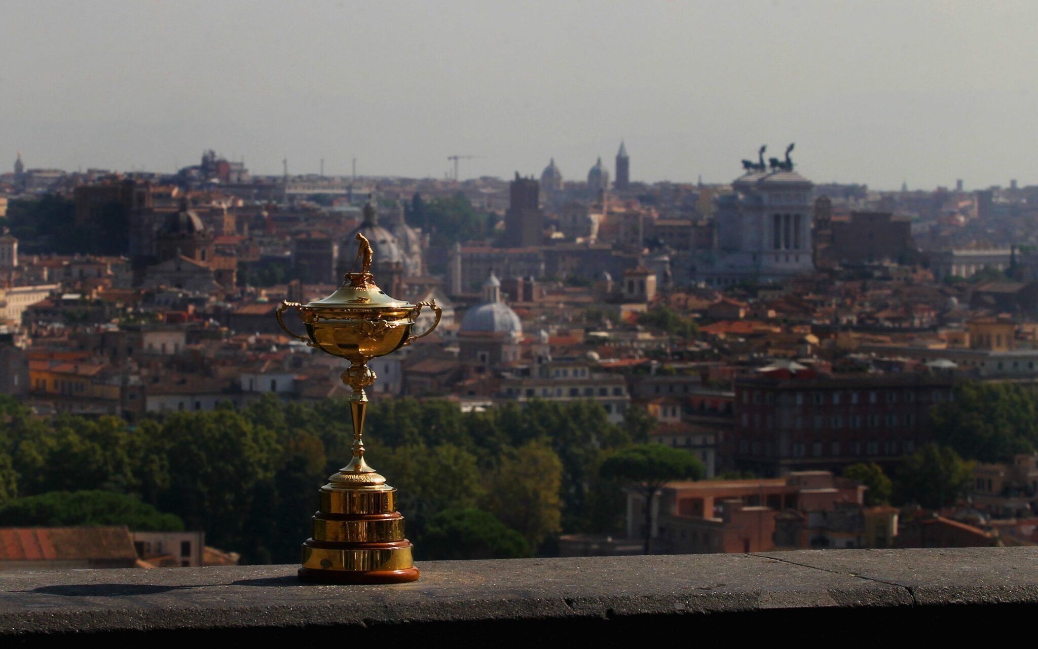 Image of the gold ryder cup place on a wall with a dusky Rome city centre in the background