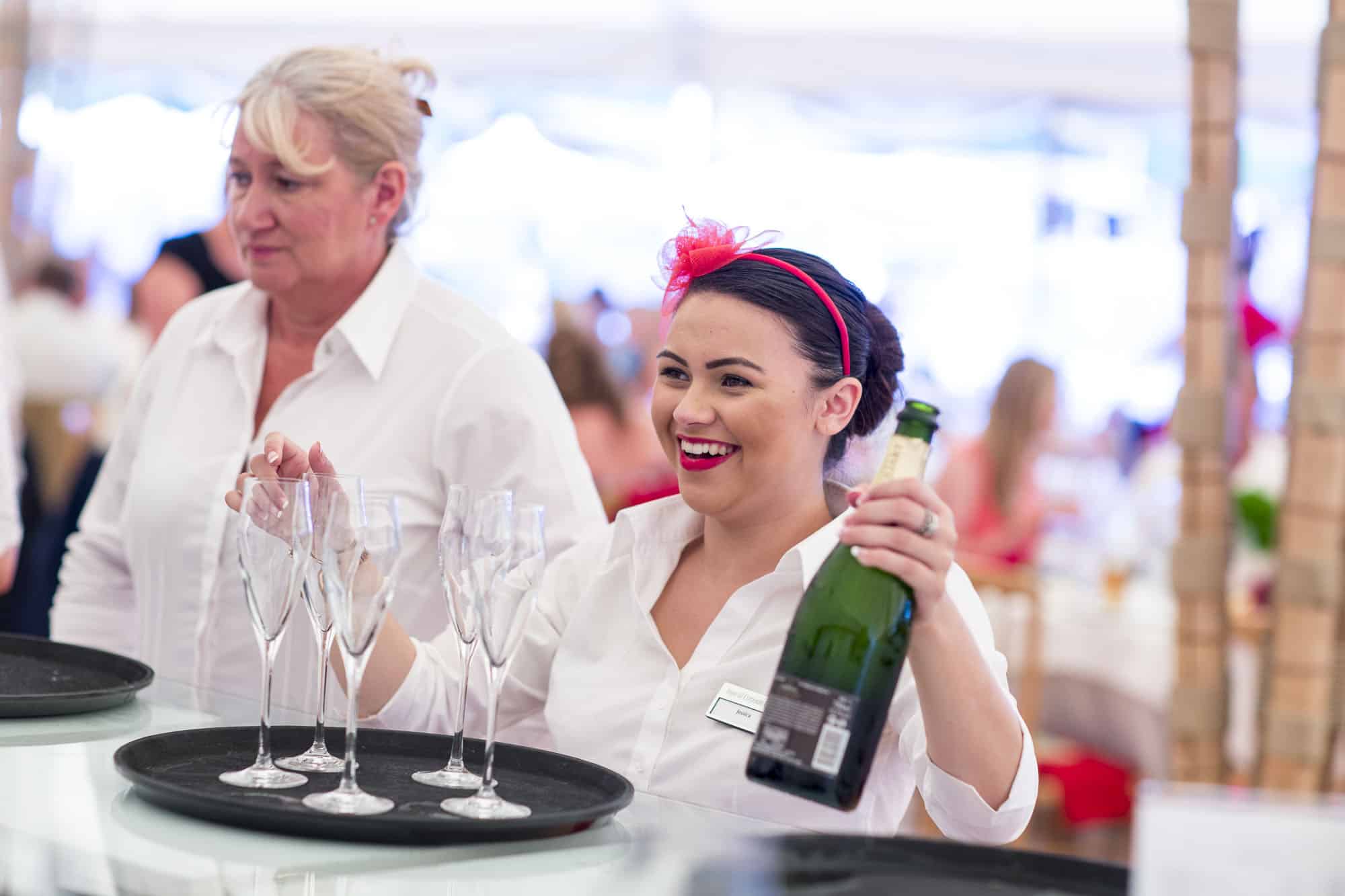 Image of waitresses smilling, holding a bottle of Champagne