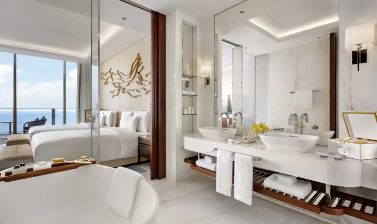 a luxury bathroom, with 2 sinks a bath tub with towels hanging over them.