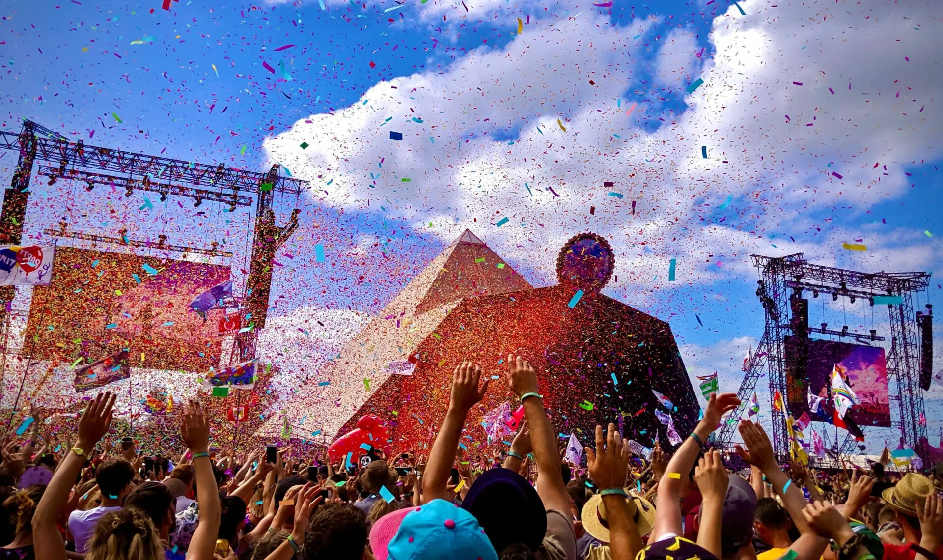 Large crowd dancing at a festival infront of a stage with colourful glitter